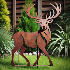 a metal sculpture of a deer standing in the middle of a yard with grass and bushes behind it