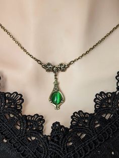 Welcome to our vintage-inspired world where elegance meets history! Dive into the allure of yesteryears with our Emerald Green Pendant Necklace, a timeless piece reminiscent of Victorian charm and historical costume jewelry. Crafted with meticulous attention to detail, this necklace features a captivating emerald green cats eye cabochon set in an elegant teardrop shaped antiqued brass pendant. Each pendant whispers tales of romance and elegance, capturing the essence of Victorian aesthetics. Emb Shoulder Necklace Emerald, Cheap Green Retro Necklace, Cheap Retro Green Necklace, Cheap Elegant Green Necklaces, Cheap Symbolic Green Jewelry, Medieval Jewelry Emerald, Luxury Green Victorian Necklaces, Cheap Green Vintage Necklace, Cheap Green Whimsical Necklaces