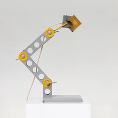 a sculpture made out of metal and yellow circles on top of a white block with wires attached to it