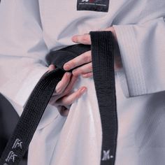 a person wearing a black belt and white shirt holding onto their hand while standing in front of the camera