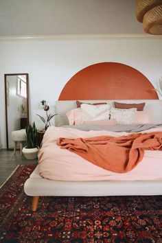 a bed with an orange headboard in a bedroom next to a rug and potted plants