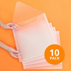 a person holding some clear plastic sheets on top of an orange surface