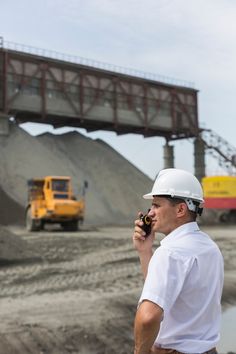 a man wearing a hard hat and holding a cell phone to his ear while standing in front of a construction site