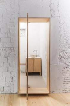 an open door leading to a bathroom with a sink and mirror on the wall, in front of a white brick wall