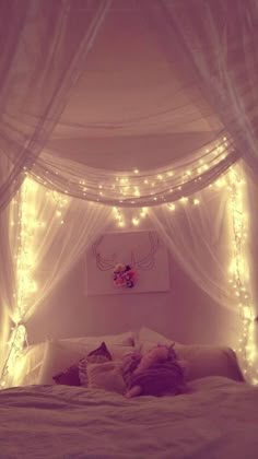 a bed with white sheets and lights on the headboard is lit up by fairy lights