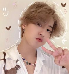 a person making a peace sign while wearing a white shirt and silver necklace with hearts on it