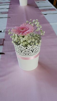 pink and white flowers are in a pot on a long table with purple linens