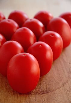 a bunch of red tomatoes sitting on top of a wooden cutting board next to each other