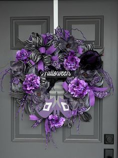 a purple and black halloween wreath on a gray door with the word halloween painted on it