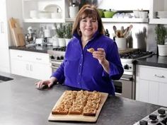 a woman standing in front of a counter holding a piece of food and pointing at the camera