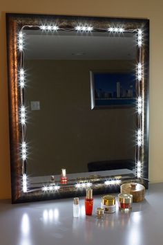 a lighted mirror sitting on top of a table next to candles and lipstick bottles in front of it