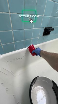 a person with blue gloves is cleaning a bathtub in the bathroom and holding a red cup