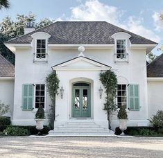 a white house with blue shutters and green doors on the front door is surrounded by greenery