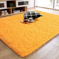 a bright yellow rug in the middle of a living room with pillows and coffee mugs on it