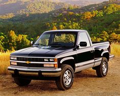 a black pickup truck parked on top of a dirt road in front of trees and mountains