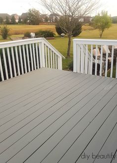 a deck with white railings and wood flooring next to a grassy area in the background