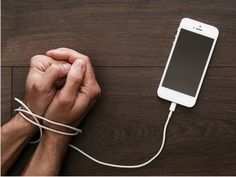 a man is plugging in to an iphone charger on a wooden table with his hands