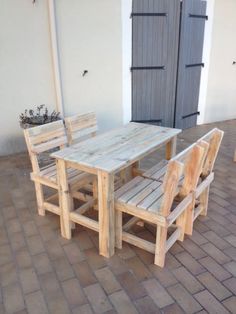 a wooden table and chairs sitting on top of a brick floor next to a building