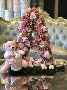 a teddy bear sitting on top of a table next to a letter made out of flowers