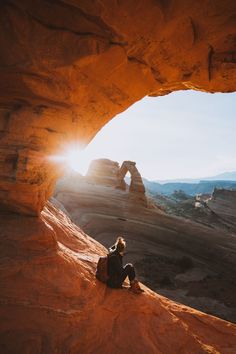 a person sitting on top of a rock near a large arch in the middle of nowhere