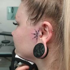 a woman with a tattoo on her ear and behind her ear is a black flower