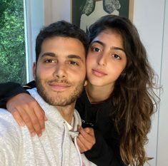 a man and woman are posing for a photo in front of a window with their arms around each other