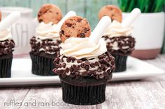 chocolate cupcakes with white frosting and cookies on top sitting on a plate