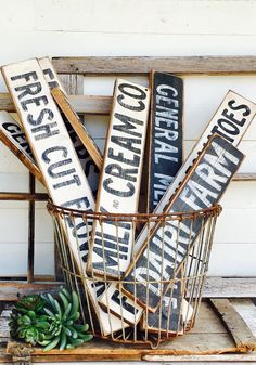 a basket filled with wooden signs sitting on top of a table next to a plant