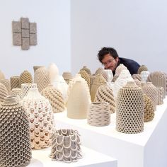 a man is looking at several vases on display in a room with white walls