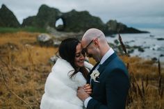 a bride and groom embrace in front of the ocean on their wedding day at cannon rocks