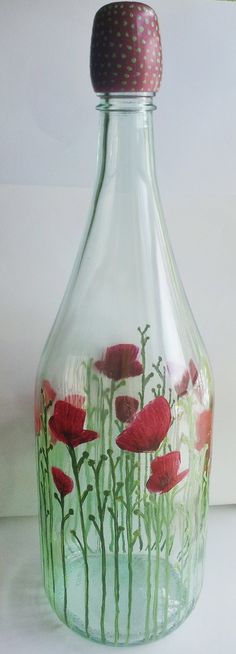 a glass bottle with red flowers painted on the bottom and green stems in the bottom