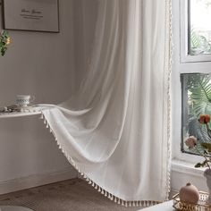 a white curtain hanging in front of a window next to a table with flowers on it