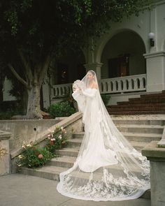 a woman in a wedding dress and veil standing on some steps with flowers around her