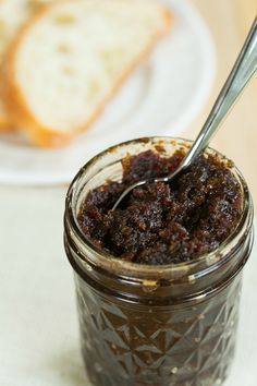 a spoon in a jar filled with jam next to a slice of bread on a plate