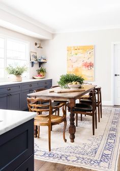 a dining room table and chairs in front of a painting on the wall with potted plants