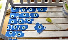 blue flowers are painted on the back of a wooden chair with paintbrushes next to it