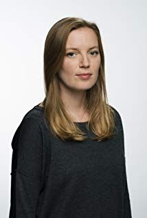 a woman standing in front of a white background wearing a black shirt and jeans with her hands on her hips