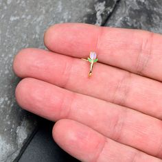 a person's hand is holding a tiny ring with a flower on the middle