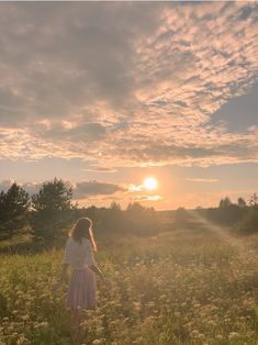 a girl in a field with the sun setting behind her and clouds above her head