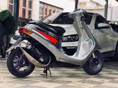 a silver scooter parked in front of a car on a checkered floor