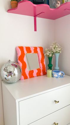 a white dresser topped with a mirror next to a shelf filled with books and vases