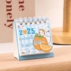 an orange calendar sitting on top of a wooden desk next to a pen and pencil holder