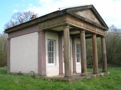 an old building sitting in the middle of a field with columns on it's sides