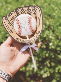 a hand holding a baseball lollipop with a ribbon around it's end