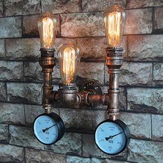 two light bulbs are attached to a brick wall with pipes and gauges on it