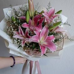 a bouquet of pink lilies and baby's breath is wrapped in white paper