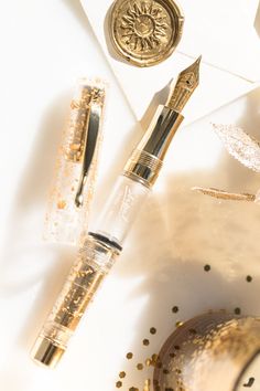 a pen and some gold confetti on a white surface with other items around it