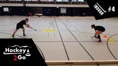 two men are playing hockey on an indoor court with yellow cones and orange balls in the foreground