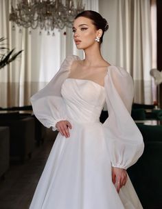 a woman in a white wedding dress standing next to a chandelier