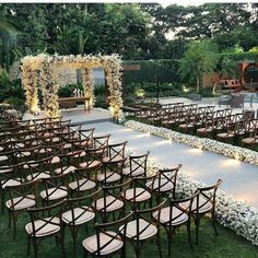 an outdoor ceremony setup with chairs and flowers on the aisle, surrounded by greenery